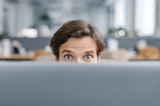 Eyes of shocked man peeking over computer