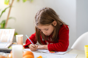 Pretty girl in pajamas sitting at table in kitchen doing homework with focus. She is concentrating...