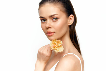 Young woman with delicate flower posing gracefully, showcasing natural beauty and simplicity in a bright, airy setting with soft tones.