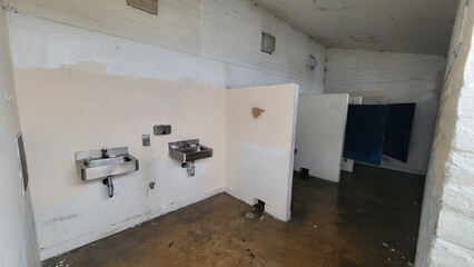 Lacking proper care public restroom facility with wet floors, stainless hand sinks, dirty lights, neglected painted walls and doors with broken locks, South Pacific Beach, San Diego, California