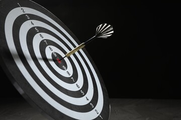 Targeting. Dart board with arrow on dark background, closeup. Space for text
