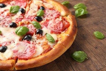 Tasty pizza with salami, cheese, basil and olives on wooden table, closeup