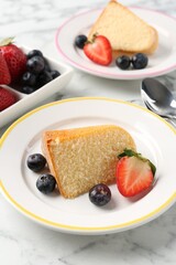 Pieces of tasty bundt cake with berries on white marble table, closeup