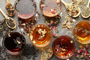 Aromatic herbal tea in glass cups, dry leaves and flowers on grey table, flat lay