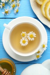 Delicious chamomile tea in cup, fresh flowers, lemon and honey on light blue wooden table, flat lay