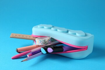 Different stationery in pencil case on light blue background, closeup