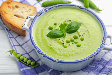 Tasty pea cream soup with basil served on white wooden table, closeup