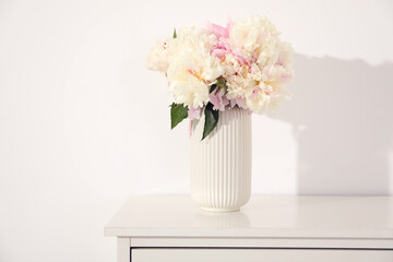 Bouquet of beautiful peonies on table near white wall
