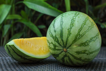 Whole and cut yellow watermelons on wicker table outdoors, closeup