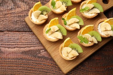 Delicious dessert. Tartlets with fruits and mint on wooden table, top view. Space for text