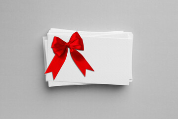 Blank gift card with red bow on light grey background, top view. Mockup for design