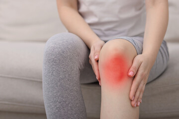Woman suffering from pain in knee on sofa at home, closeup