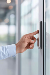 Hand pressing a button on a glass door to enter a modern office space in a bright and airy environment