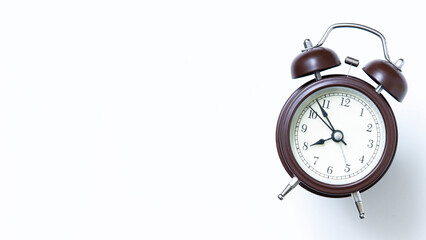 Horizontal close up photo of a brown alarm clock with a white face showing the time of 08.00 isolated white background