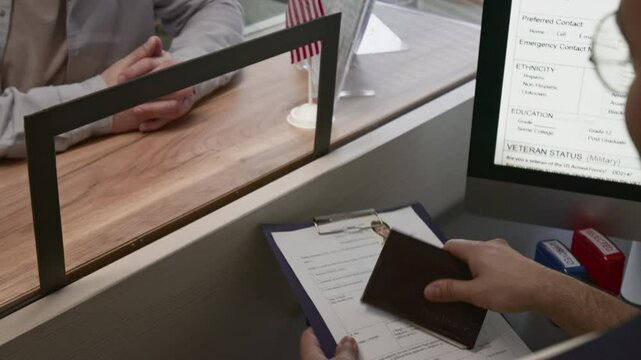 Over the shoulder view of male visa operations officer putting rejection seal in applicants passport and returning documents to him, young man feeling frustrated