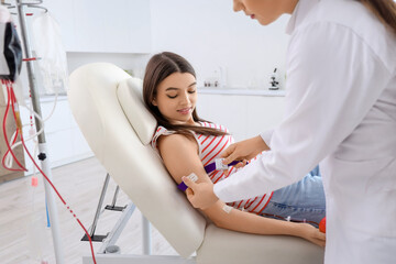 Female doctor preparing young donor for blood transfusion in clinic