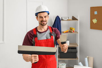 Male decorator with putty knives in room