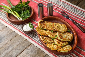 Plate of tasty zucchini fritters with sour cream on wooden background