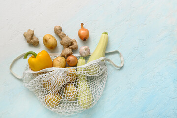 Mesh bag with different fresh vegetables on blue background