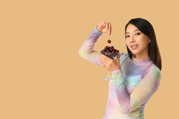 Beautiful Asian woman with sweet cherries on beige background