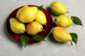 Plate with fresh pears and leaves on grey background