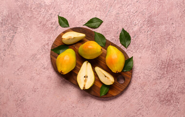Wooden board with fresh pears and leaves on pink background