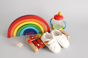 Stylish baby shoes with toys, pacifier and bottle of milk on grey background