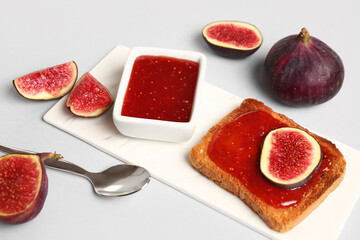 Obraz premium Board with bowl of sweet fig jam and tasty toast on white background