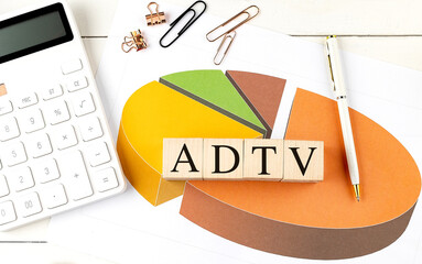 ADTV abbreviation on wooden blocks with pie chart, calculator, pen and paper clips on white office desk