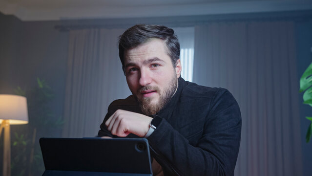 Man in dark jacket looking at camera near laptop - Powered by Adobe