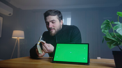 Man counting money next to tablet with green screen