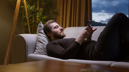 Man relaxing on sofa using smartphone at night