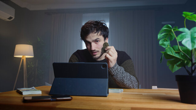 Man holds up a bitcoin while speaking to the camera in a professional home office. Investment, cryptocurrency, and wealth management