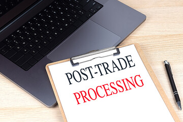 Post-trade processing text on clipboard with laptop and black pen on wooden desk