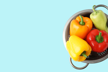 Colander with fresh bell peppers on blue background