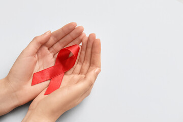 Woman with red ribbon on light background. AIDS Day concept