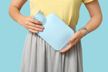 Young woman with hot water bottle having menstrual cramps on blue background, closeup