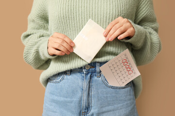 Young woman with menstrual pad and calendar on beige background, closeup