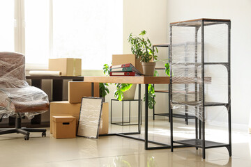 Interior of office with chair wrapped in stretch film and cardboard boxes on moving day