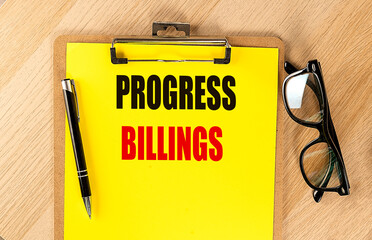 Progress billings text on yellow clipboard with pen and eyeglasses on wooden desk