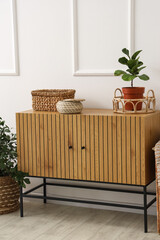 Wooden cabinet with flowerpot and wicker baskets near white wall