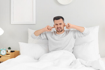 Young man suffering from loud neighbours in bedroom