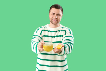 Young man with glass cup of tea and lemon on green background