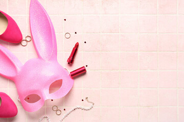 Pink bunny mask with high heel shoes, lipstick and accessories on color tile background