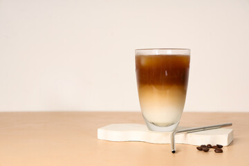 Glass of iced latte and coffee beans on beige table
