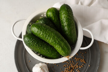 Colander with fresh green cucumbers and garlic on white background