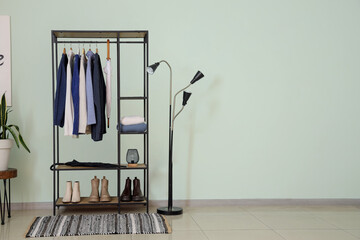 Rack with sweaters and shoes near light green wall in room