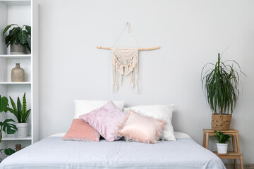 Cozy bed, shelving unit and houseplants in interior of bedroom