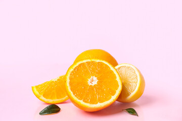 Cut oranges and lemon with leaves on pink background