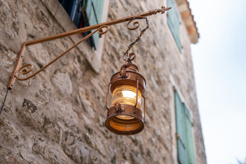 A warm, glowing lantern hangs on an old stone wall beside green shutters, reflecting rustic charm and classic architecture. perfect for themes of history, light, and vintage design.